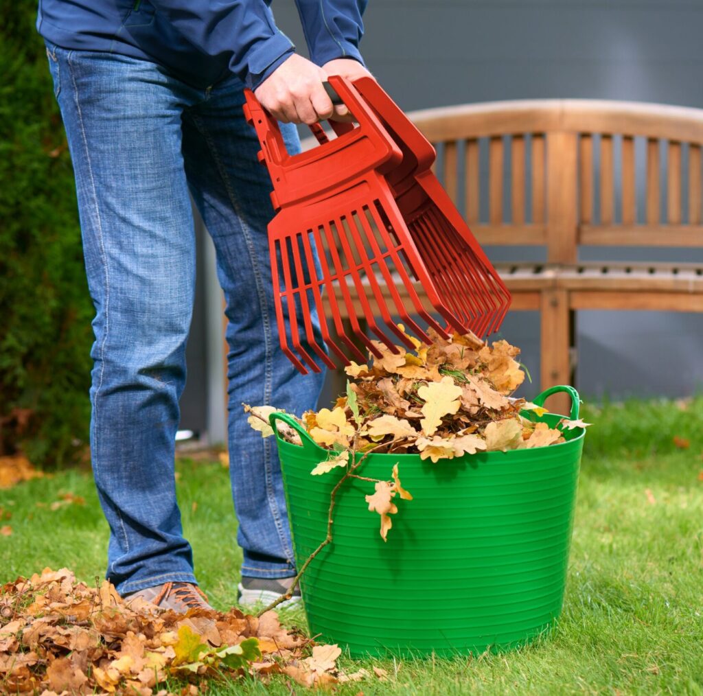Ein Mann sammelt Blätter unter einer Bank mit Hilfe des schmalen Mittelteils des WOLF-Garten Multi-Star® System-Aufsatzes LEAF RAKE 4-IN-1.